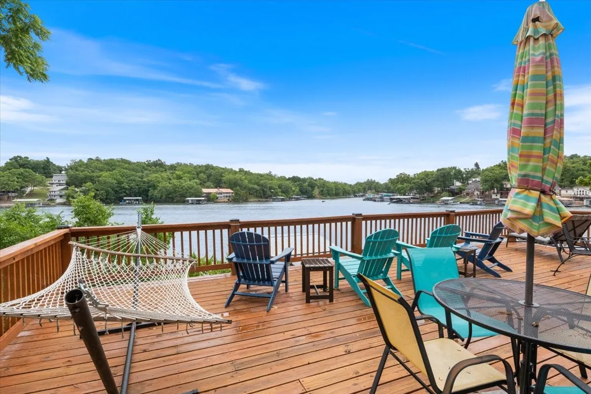 A tranquil deck scene with a hammock, comfortable deck chairs, a table under a large umbrella, and a sweeping view of the lake. The setting invites guests to relax, socialize, read, or simply soak up the calming lakeside atmosphere.