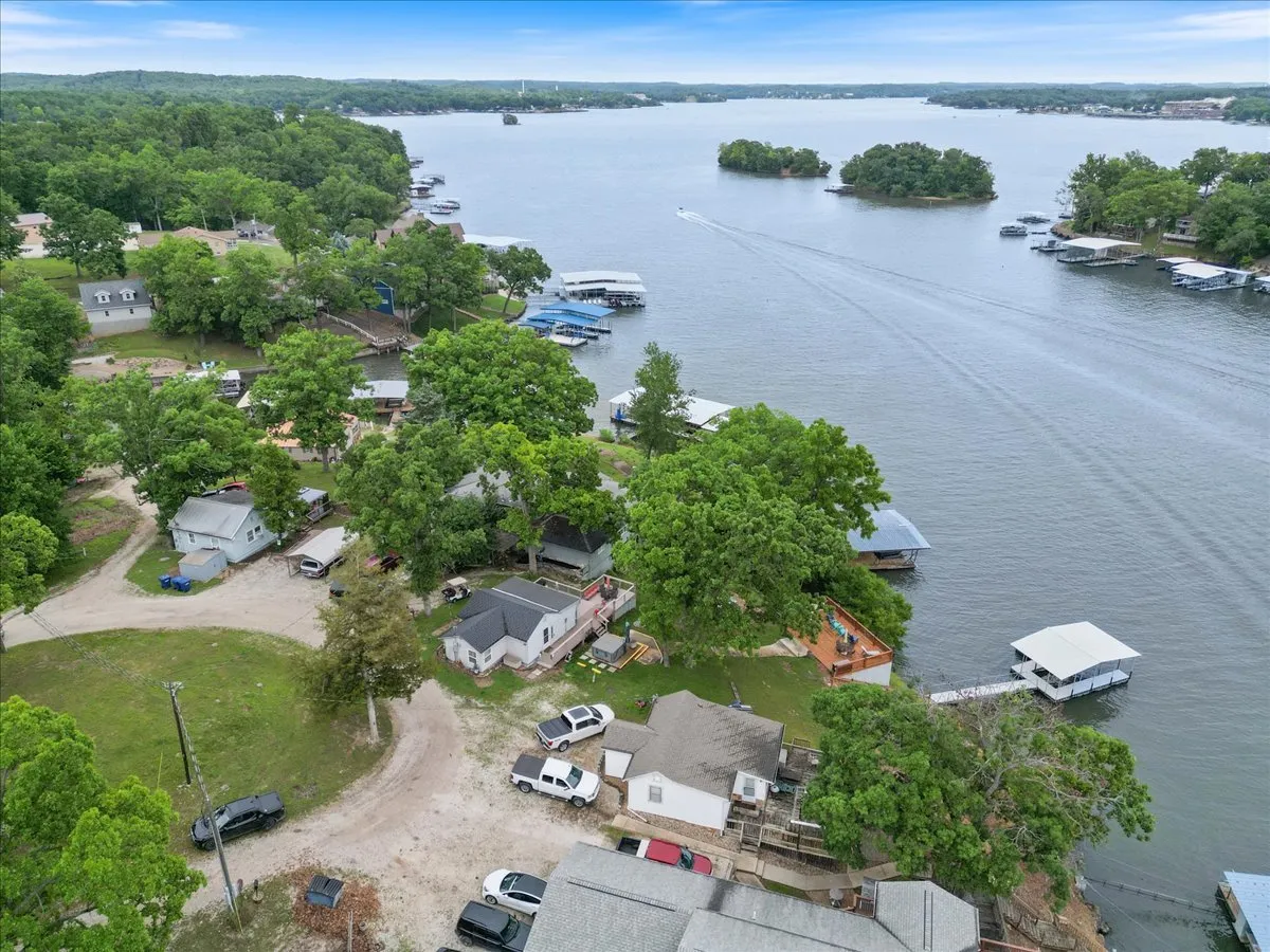 A tranquil exterior view featuring the lake, several boats, a dock, surrounding trees, and neighboring houses. The image captures a leisurely mood, highlighting the water-based activities and vibrant community life along the lake.