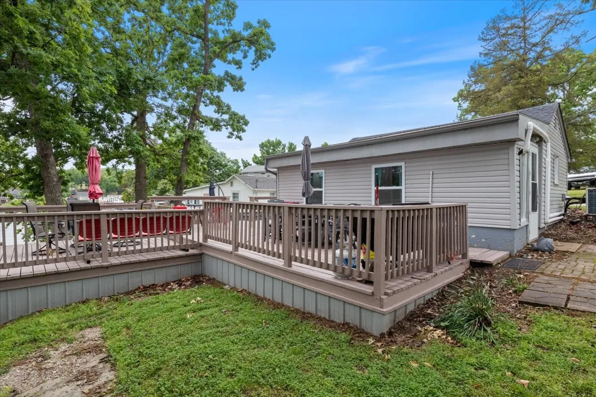 A deck area surrounded by trees, featuring outdoor seating and a patio umbrella. The scene suggests relaxation and opportunities for casual outdoor dining or enjoying fresh air with pets on a leash.
