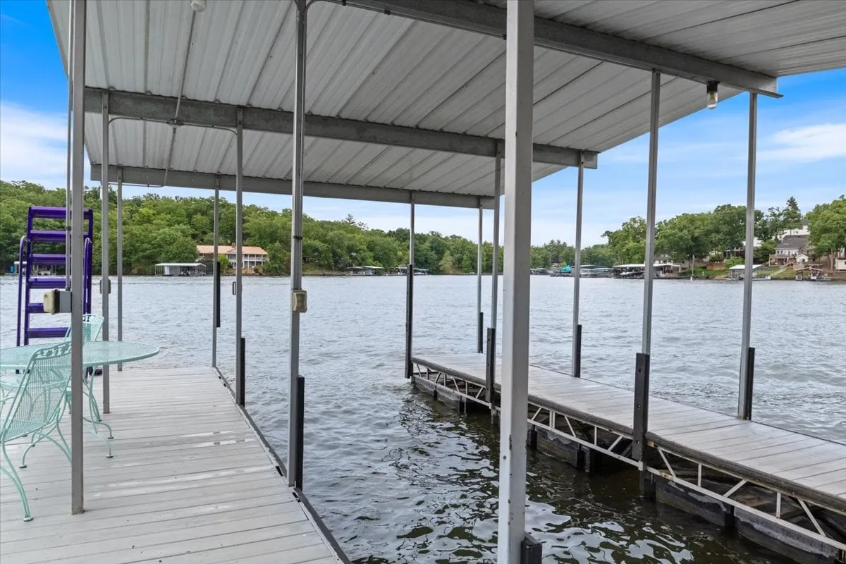 A wide shot of the private dock extending into the lake, surrounded by lush greenery. Boats are moored at the dock, and the scene is peaceful, with calm water and soft sunset light. The swim platform and dedicated boat slip are visible, highlighting access for boating and fishing.