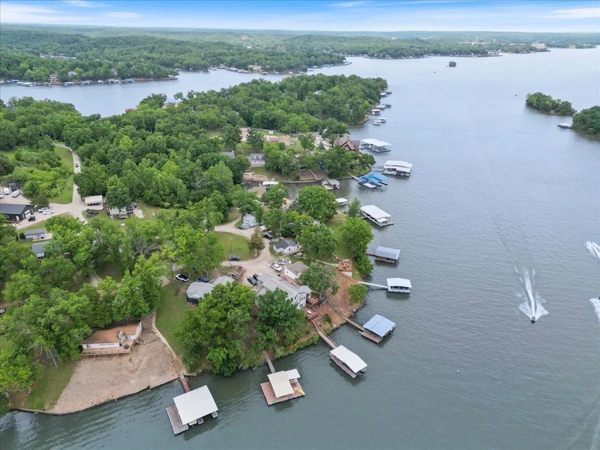 A scenic view capturing lush greenery surrounding the lake, with boathouses, docks, and a picturesque shoreline. The image exudes a serene and inviting atmosphere, showcasing the natural beauty of the Lake of the Ozarks and its recreational opportunities.