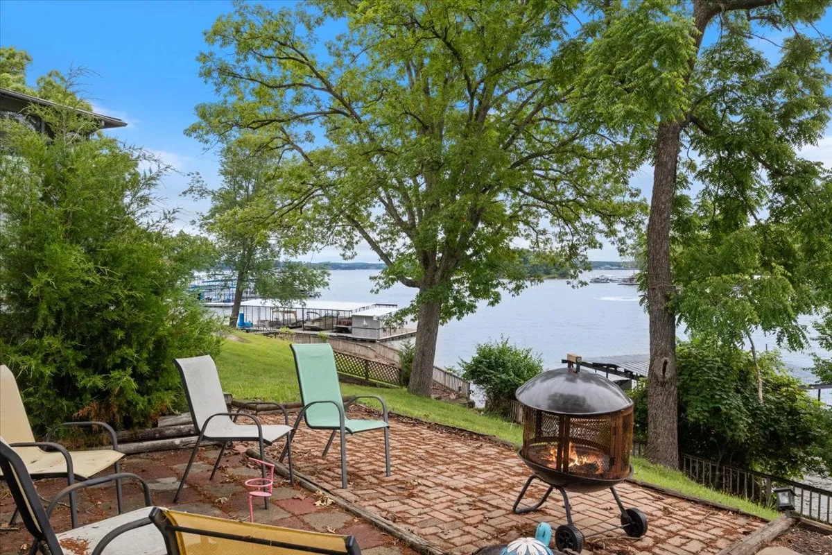 This exterior image features a cozy fire pit seating area facing the lake, surrounded by trees. The scene is inviting for evening gatherings, making s'mores, and sharing stories under the stars.