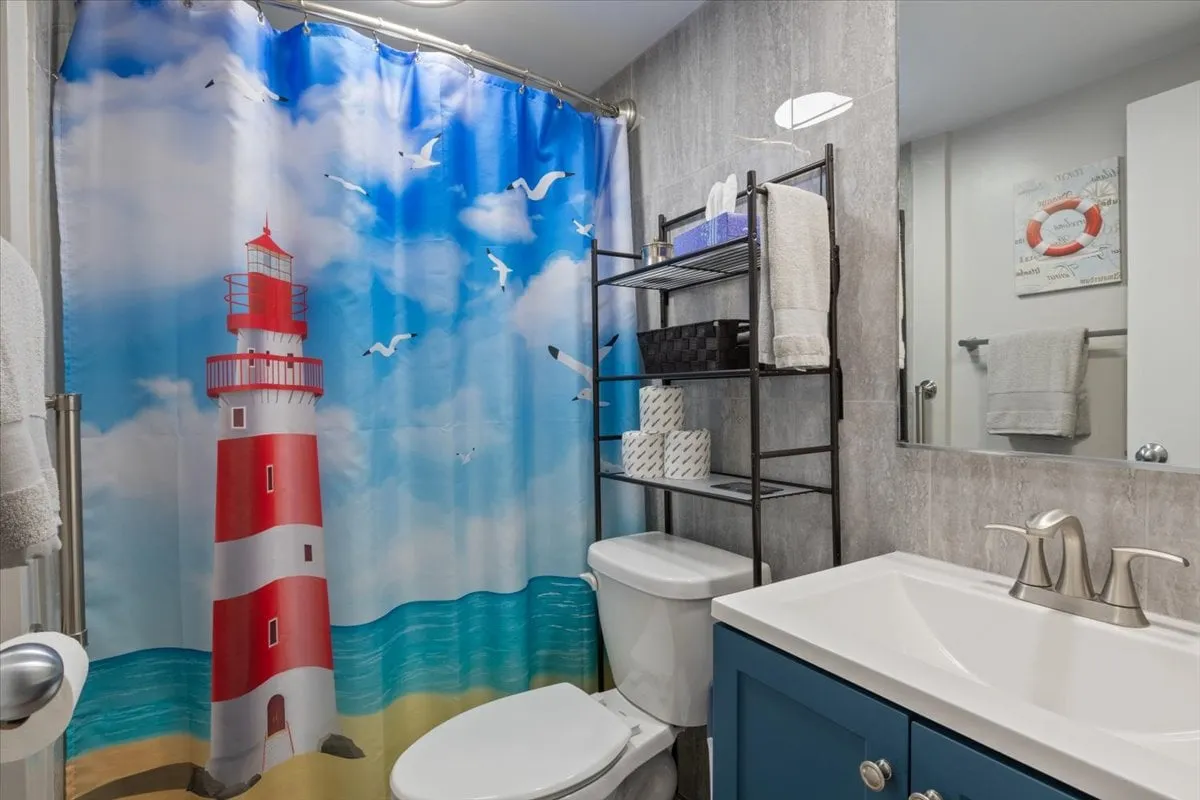 A bright, inviting bathroom with a playful lighthouse-themed shower curtain, blue cabinetry, and modern fixtures. The space feels fresh, playful, and practical—ideal for unwinding and refreshing after a day outdoors.