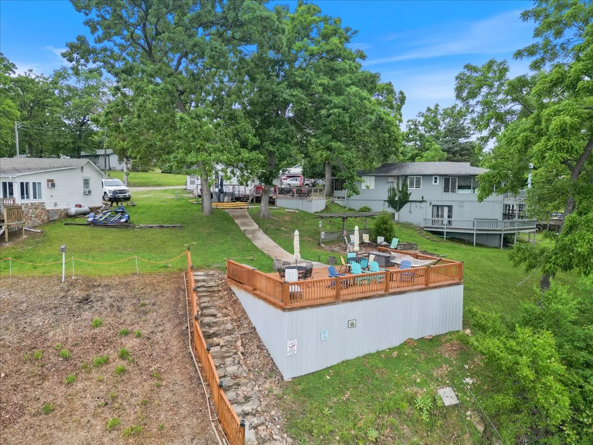 An exterior shot of a comfortable deck area with outdoor seating, a pathway leading directly to the water, and lush greenery all around. The inviting space hints at cozy gatherings, peaceful mornings, and easy access to the lake.